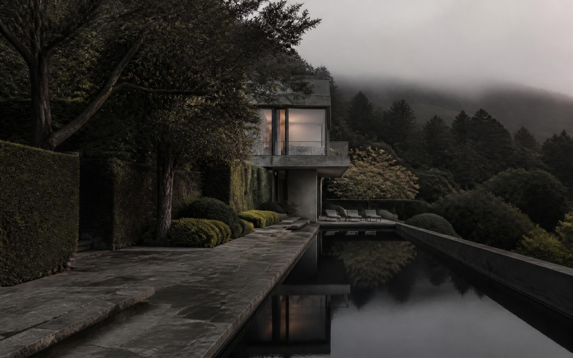 Dusk view of a hillside garden with clipped hedges and a still reflecting pool beside a concrete house